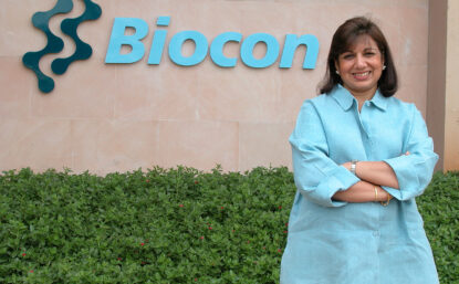Photo of Kiran Mazumdar-Shaw standing in front of the Biocon building.