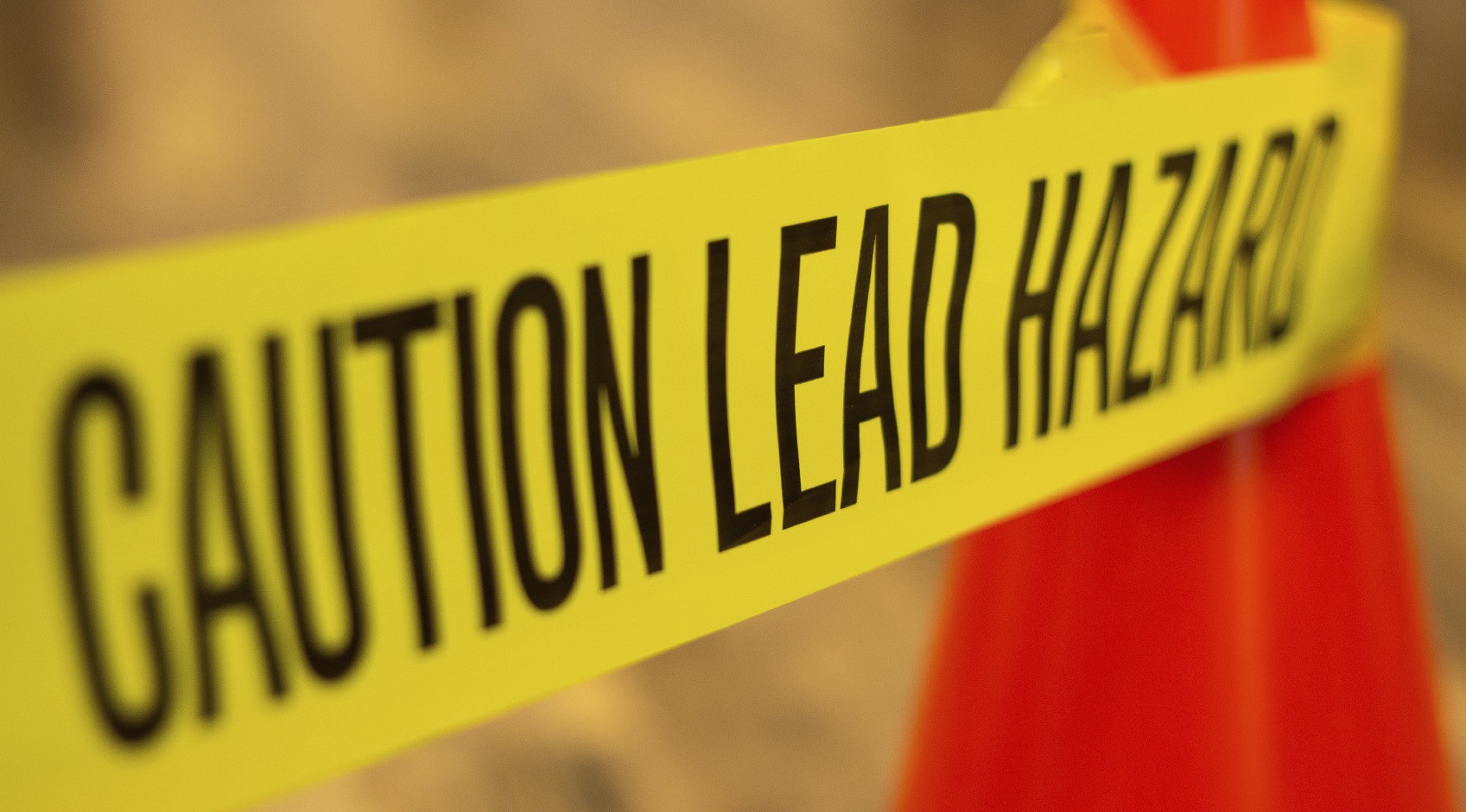 Yellow hazard tape attached to an orange cone that reads "Caution lead hazard" in all caps.