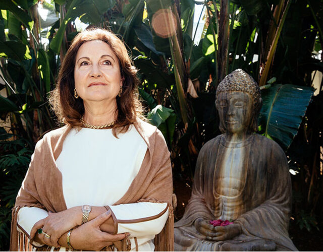 Photograph of Magda Marquet, in a garden, next to a Buddha statue.