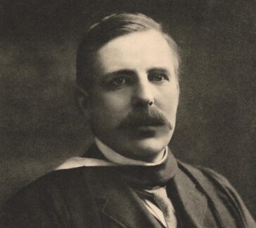 Rutherford with a thick mustache wearing a dark three-piece suit