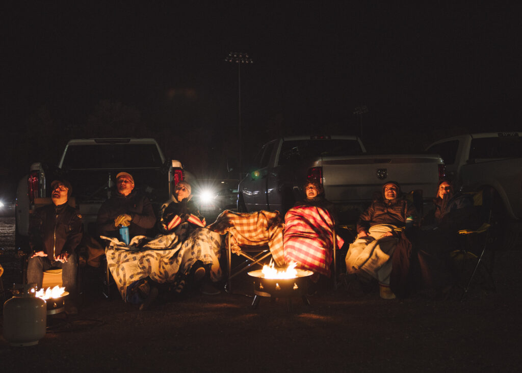 Group of people seated around fire in the dark looking to the sky