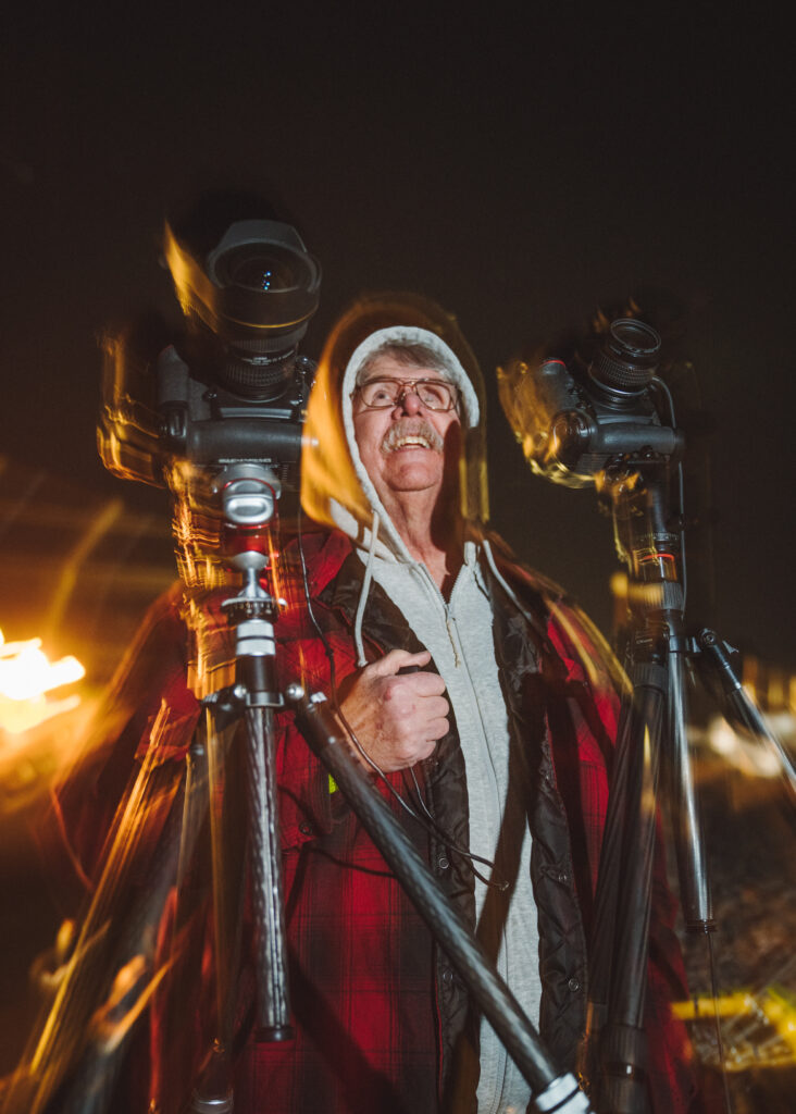 Older man in warm clothes looking to night sky with two cameras on tripods