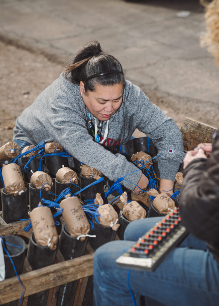 Crouching woman reaching around a large array of pyrotechnics