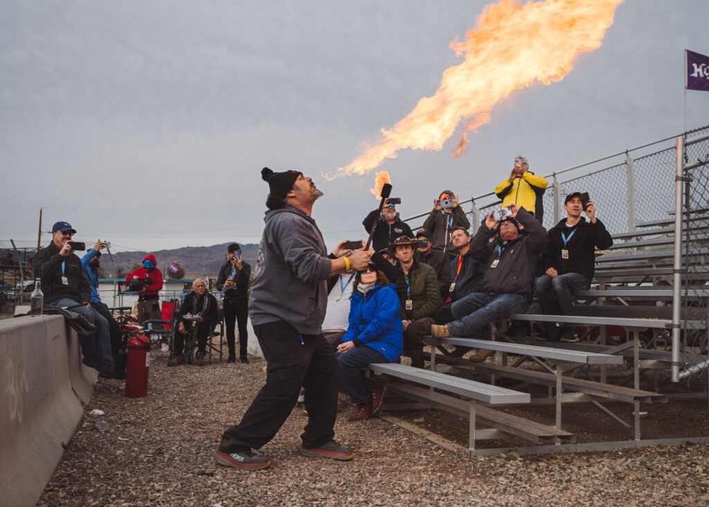 Man breathing fire in front of a small crowd seated on bleachers