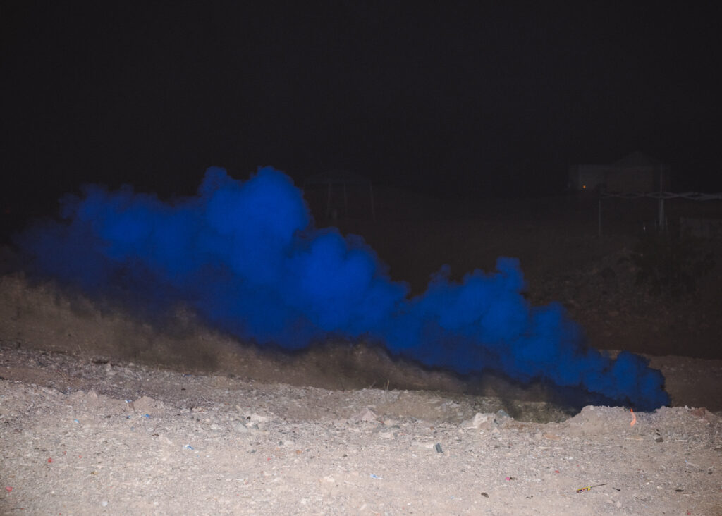 Abstract photo of a bright blue cloud of smoke in dark with lit desert floor