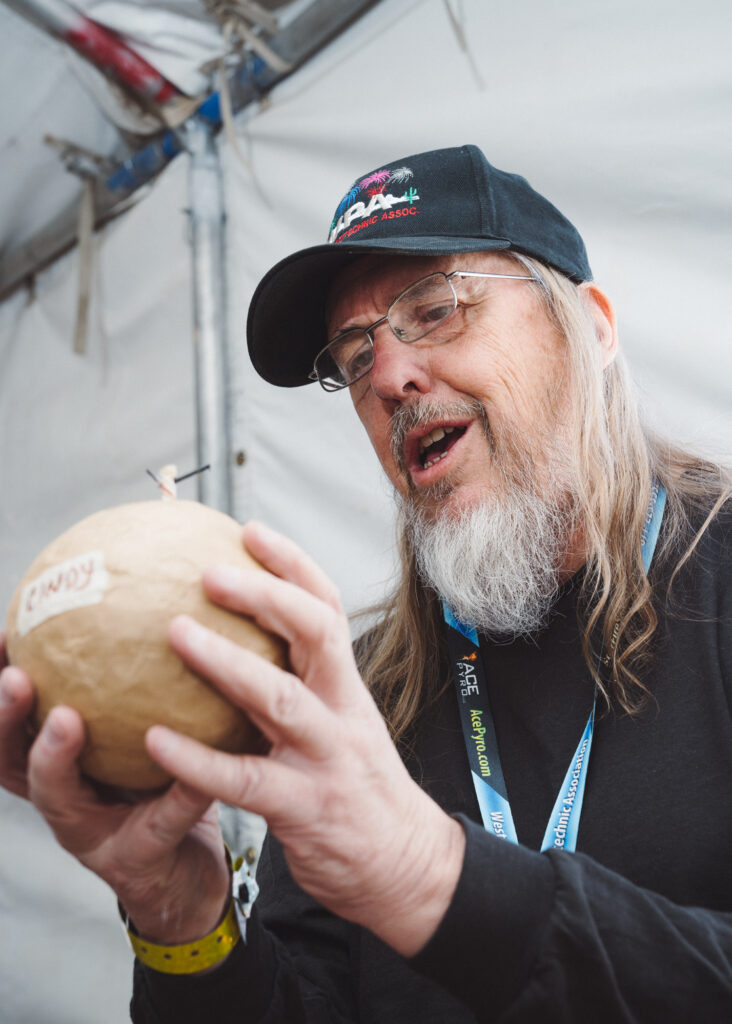 Man in ball cap with long white beard holding a large, paper-wrapped ball in his hands