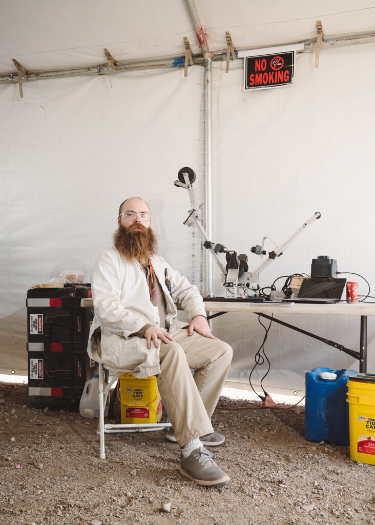Portrait of seated man in tent with large beard wearing lab coat