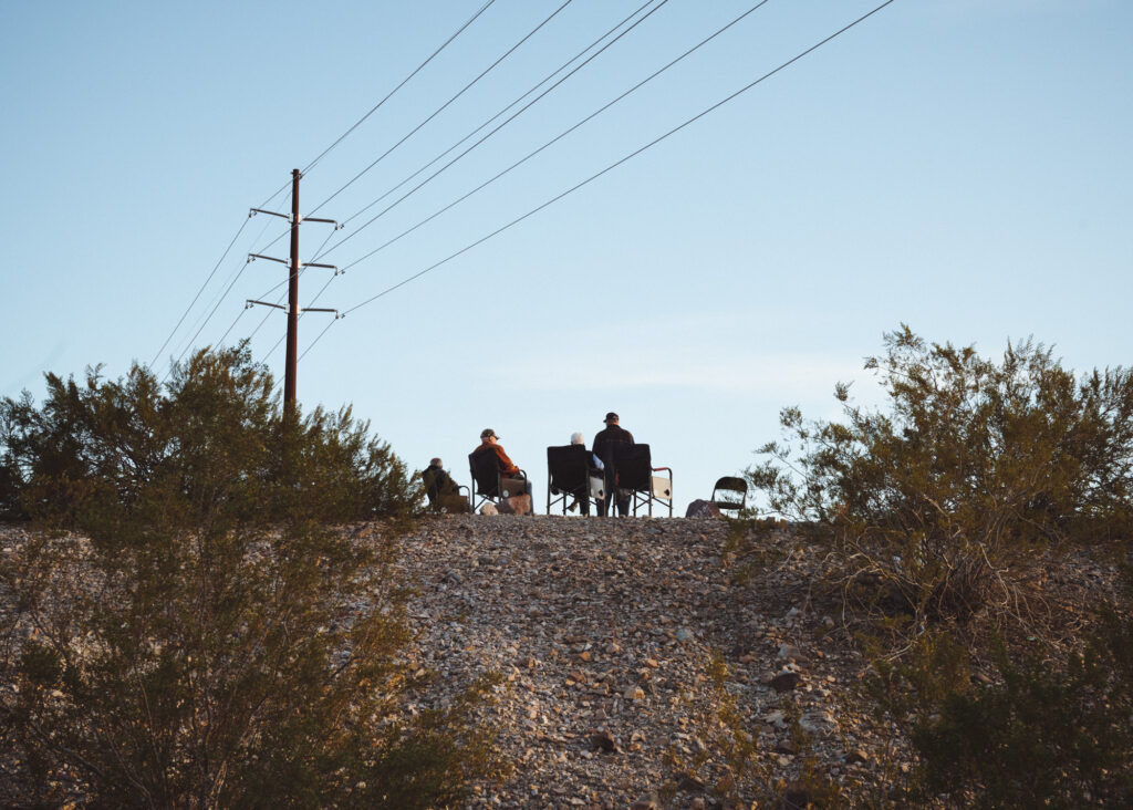 Distant photo of a small group seated on a hill under power lines at dusk