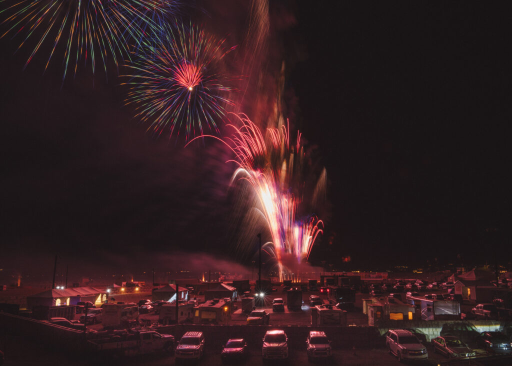 Landscape photo of large fireworks display with cars and structures below