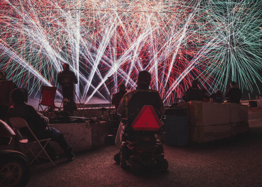 Photo of a bright fireworks display with a the silhouette of a person in a wheelchair in the foreground