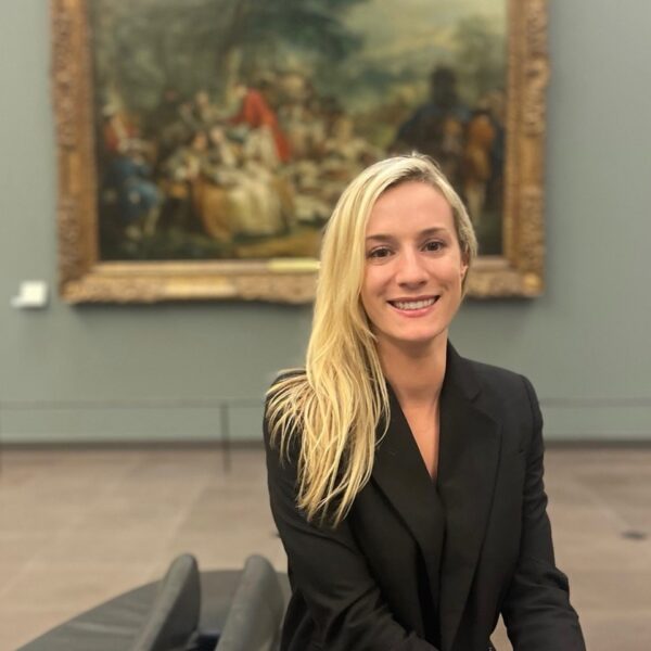 Delanie in black suit in front of a painting at a museum