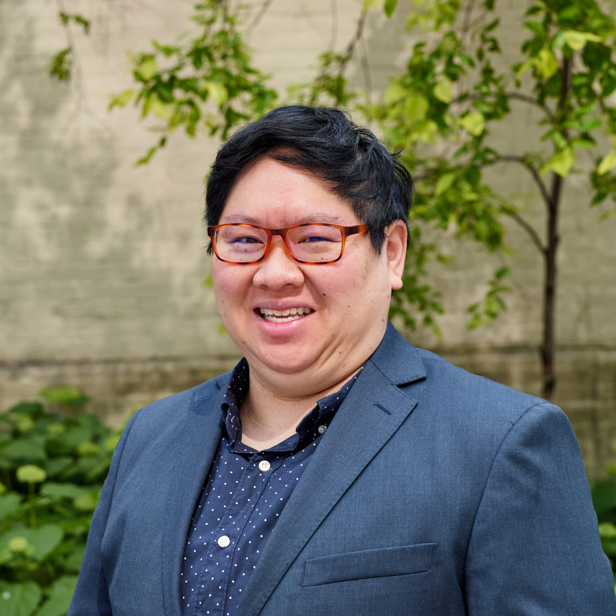 Sheu, outdoors, smiling, wearing glasses, white-on-navy polka dot shirt and blue blazer