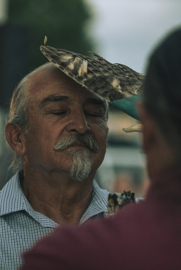 Close up of a man with eyes closed having a bundle of feathers placed on his head