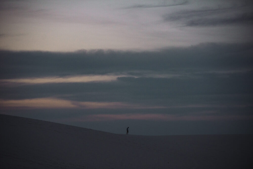Silhouette of man walking on sand dunes beneath a purple dusk sky