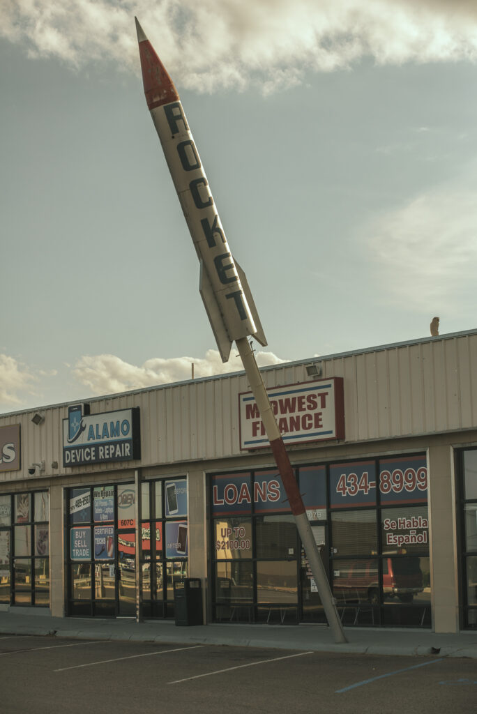 Strip mall storefronts with a large model rocket out front