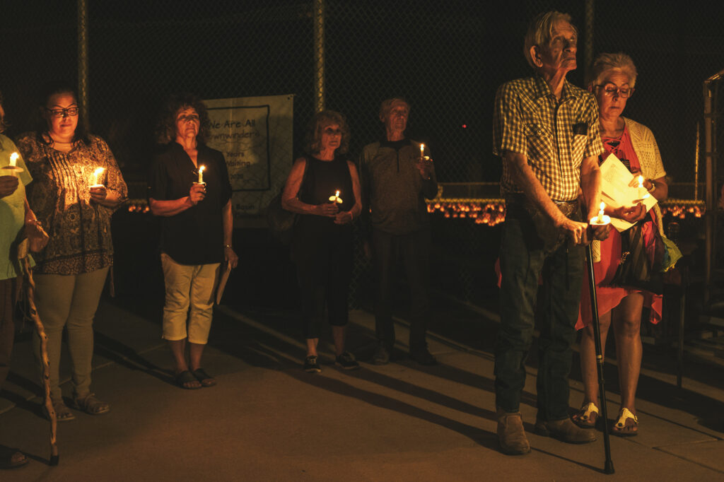 Un grupo de personas de pie en la oscuridad al aire libre con velas encendidas