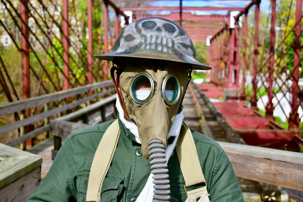 Photograph of person standing on railroad trestle wearing an early 20th century gas mask