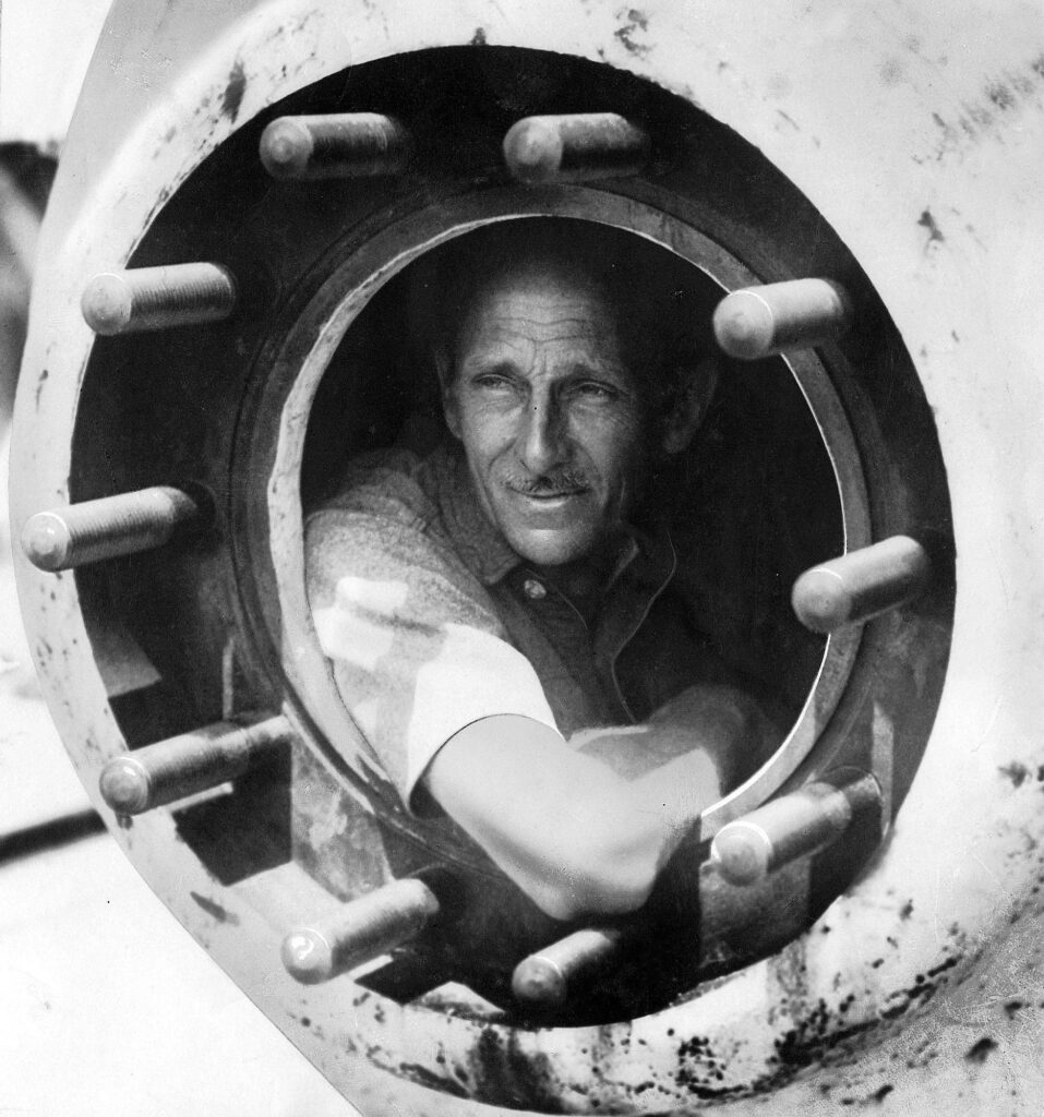 Black and white photo of a man peering out a porthole