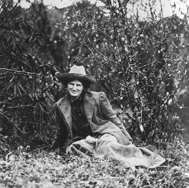 Black and white photo of woman in hat sitting in brush