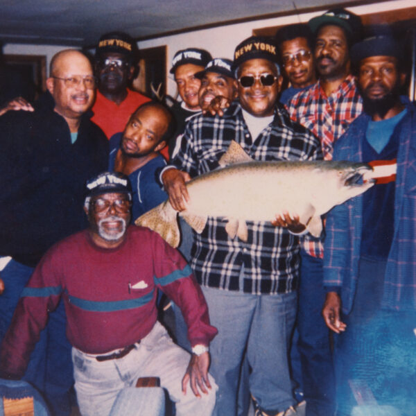 Group of eleven older men posing with a large taxidermy fish