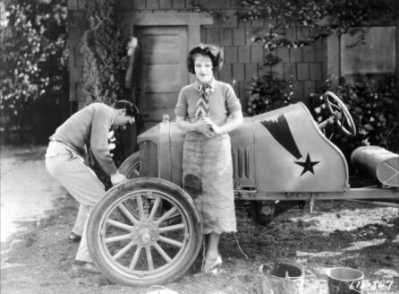 Clara Bow in front of a car being repaired
