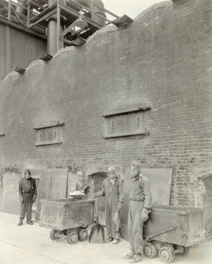 Black and white photo of men in protective equipment in front of a brink wall