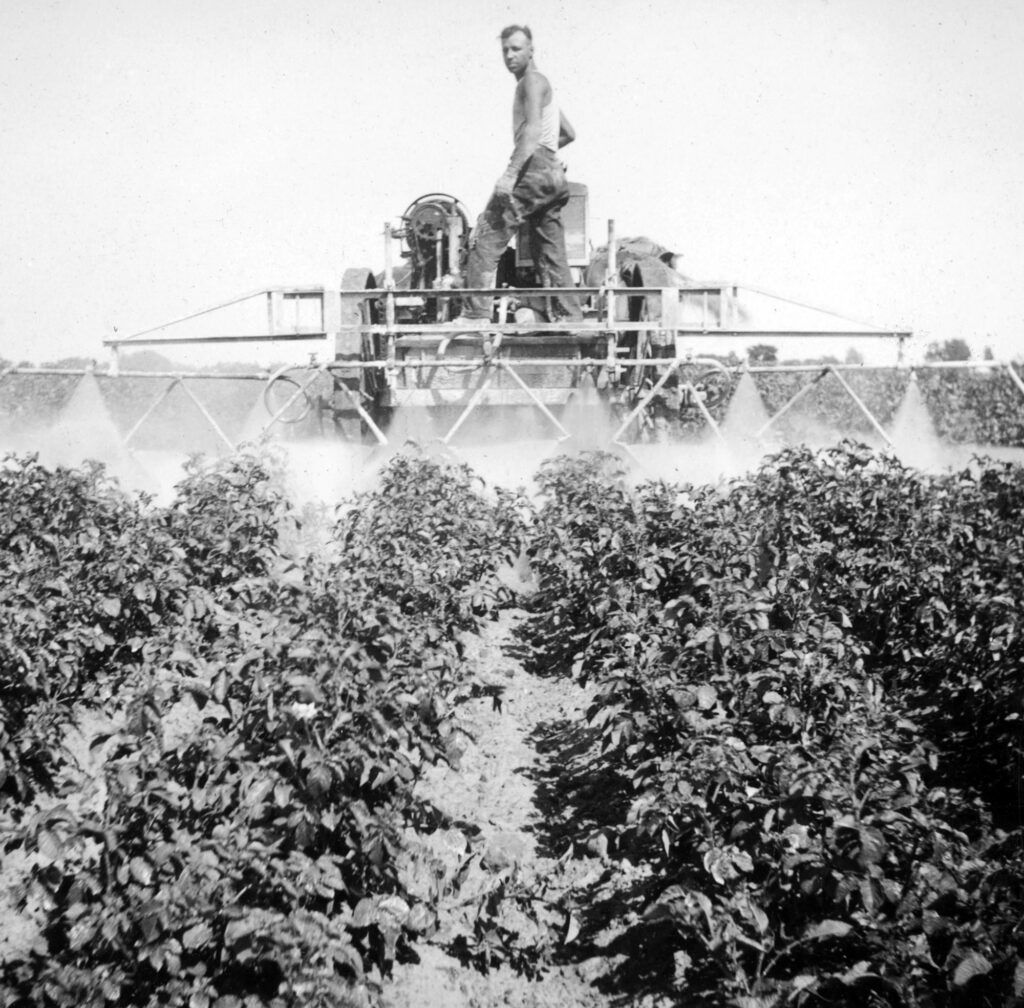 Black and white photo of a man on a spraying tractor in a field