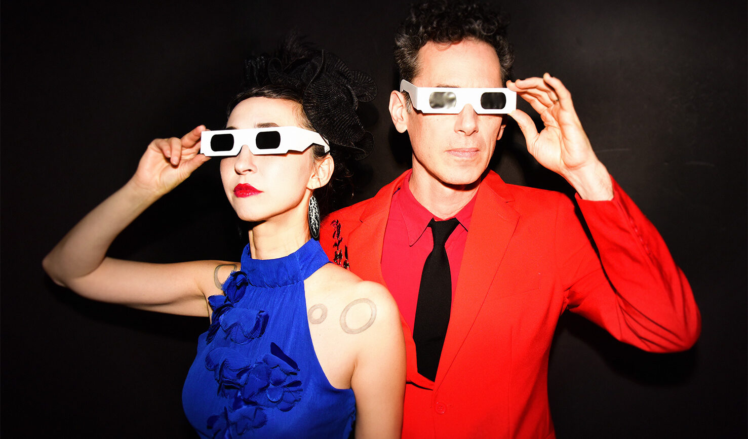 Ellia Bisker and Jeff Morris wearing eclipse glasses in a dark studio