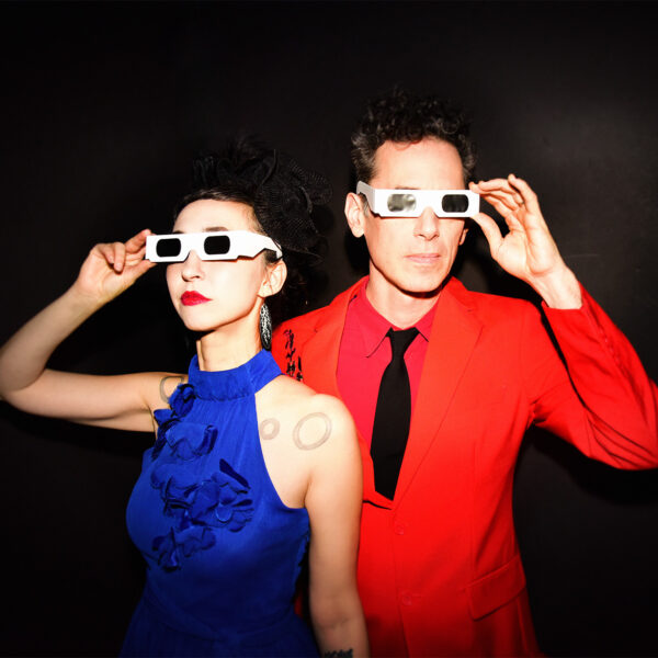 Ellia Bisker and Jeff Morris wearing eclipse glasses in a dark studio
