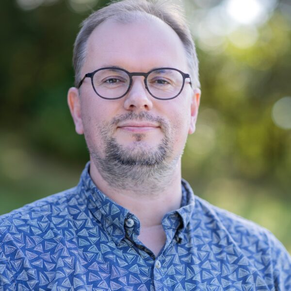 Finn Arne Jørgensen outdoors, wearing glasses and blue collared patterned shirt