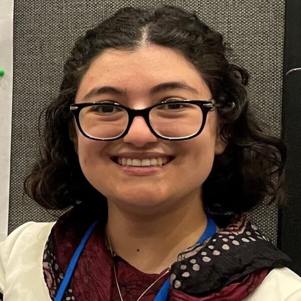 Samantha Nadel, smiling, wearing glasses, maroon and off-white top, blue lanyard