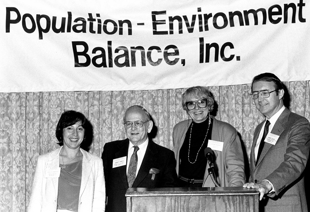 Black and white photo of four people standing in front of a dais