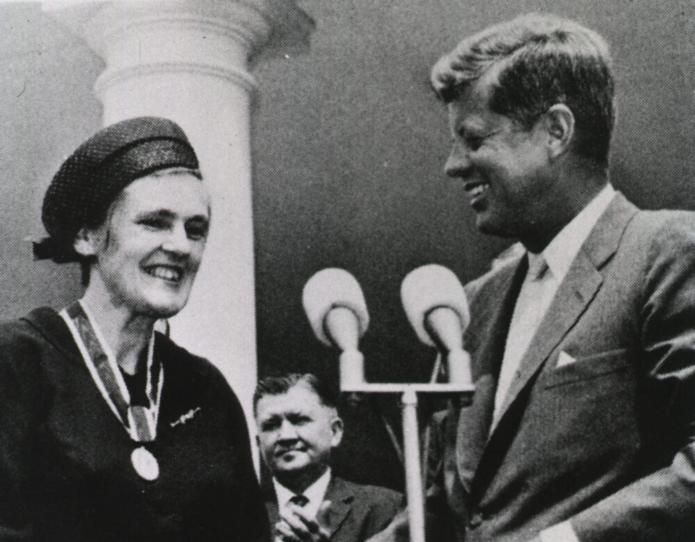 President Kennedy stands in front of microphone with Frances Oldham Kelsey