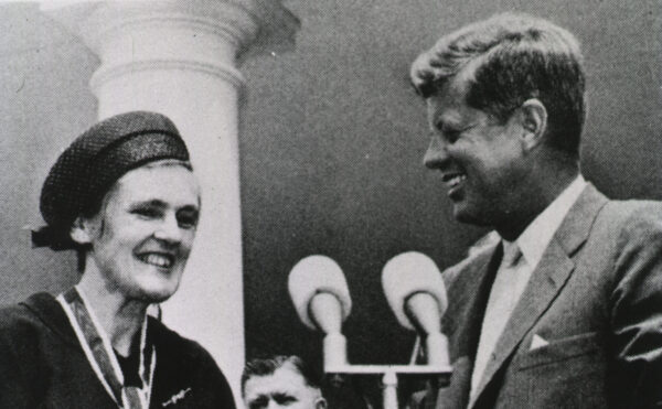 President Kennedy stands in front of microphone with Frances Oldham Kelsey