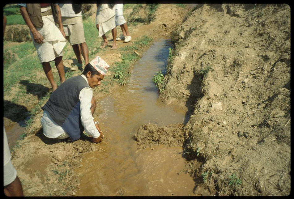 Color photo of a well-dressed crouching man with his hands in a muddy trench