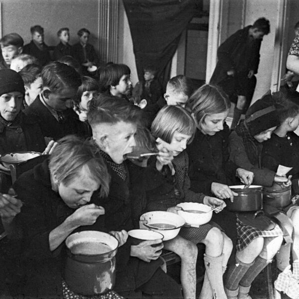 Black and white photo of dozens of children sitting with bowls of soup