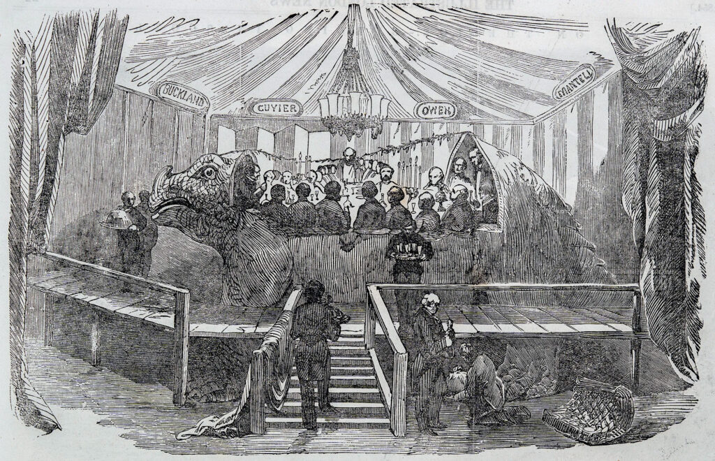 A newspaper illustration showing a group of men seated at a dinner table inside a large animal model, surrounded by a platform where servers are at work