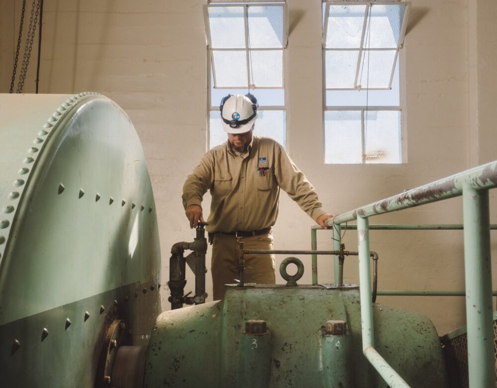 Man in hardhat and work clothes turning valve on a machine