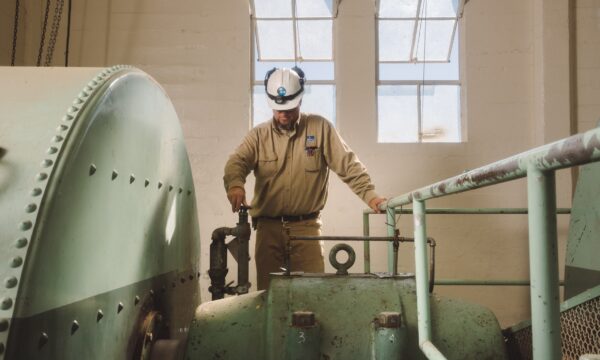 Man in hardhat and work clothes turning valve on a machine