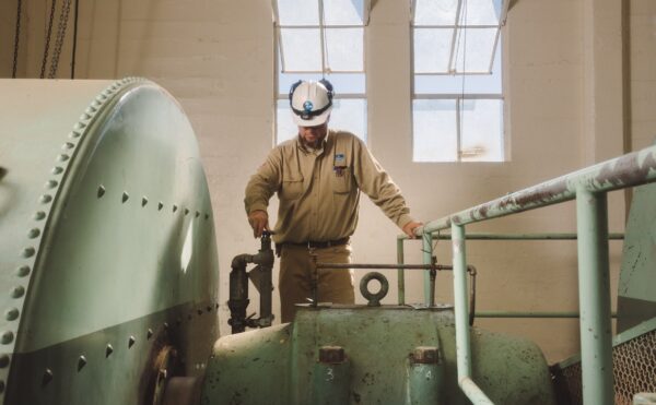 Man in hardhat and work clothes turning valve on a machine