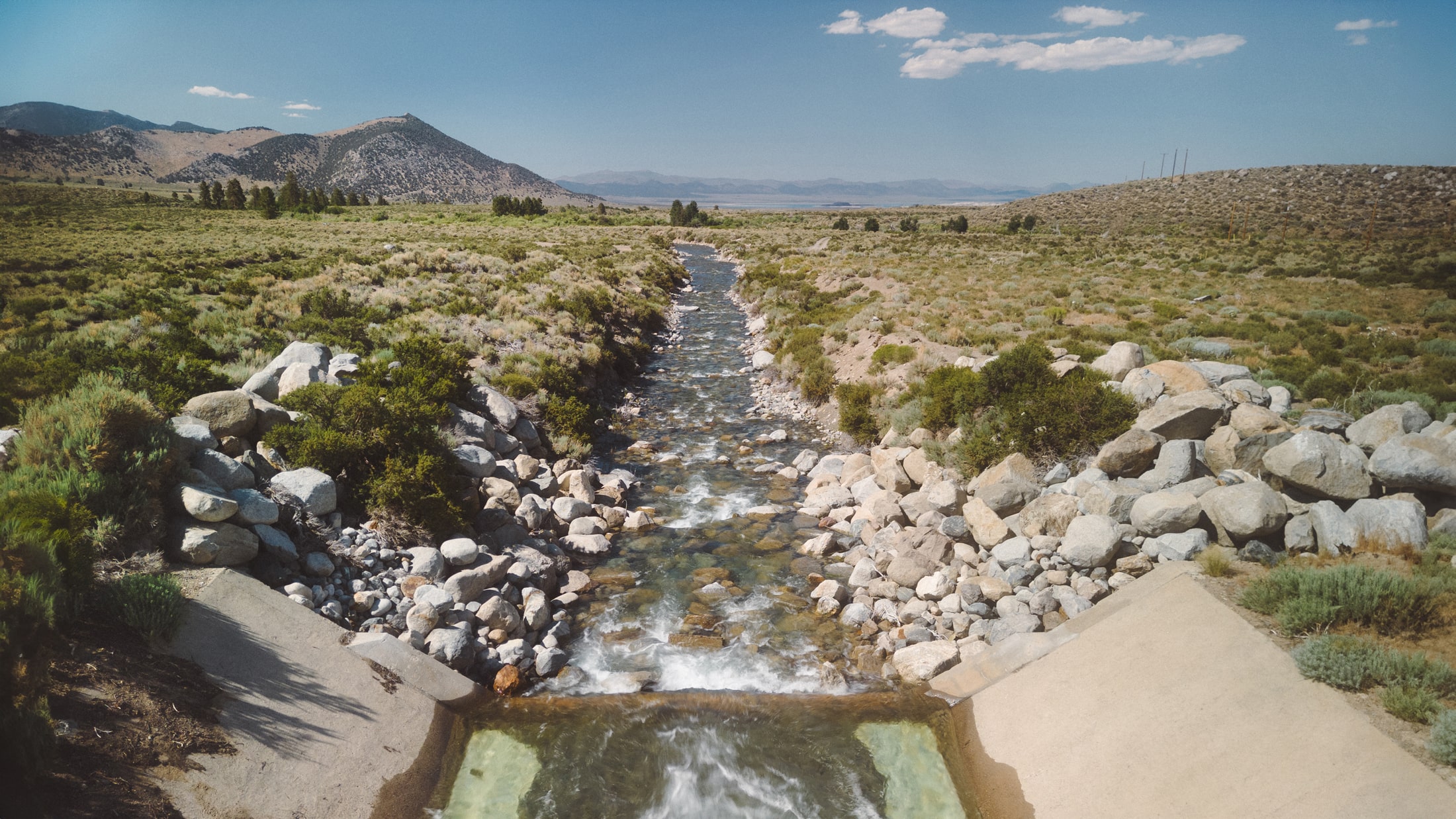 Rocky stream running through a scrubby mountain valley on a sunny day