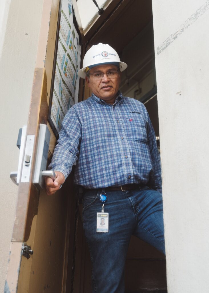 Man in glasses and hardhat holding open a door