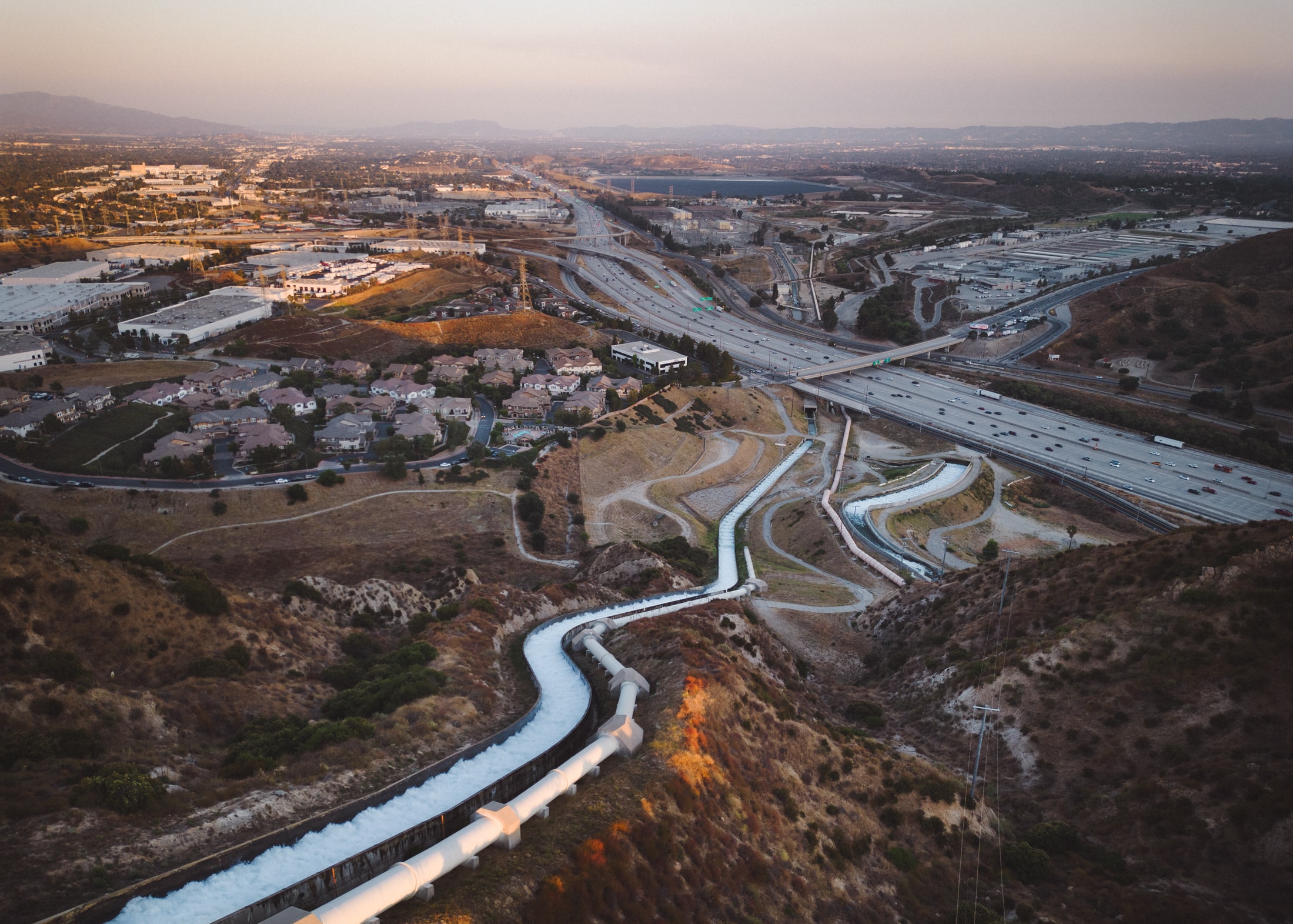 Aerial photo of water cascading down a mountainside with piping, interstate highways and housing developments in the background