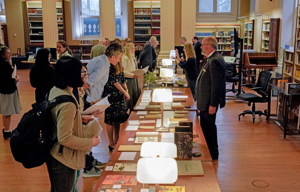 gathering in library looking at books displayed on a long table