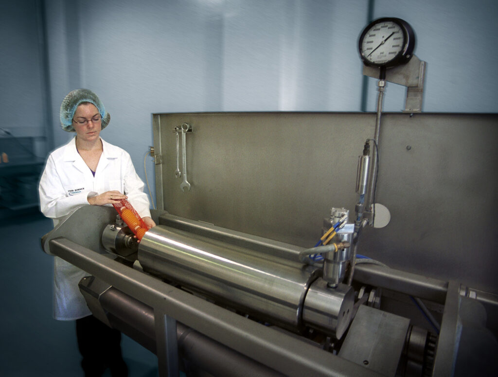 Woman in lab coat and hair net loading a long stainless-steel machine