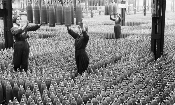 Old photo of women on a factory floor surrounded by munitions shells