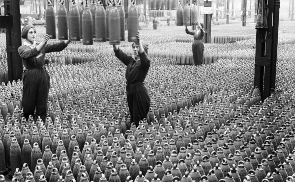 Old photo of women on a factory floor surrounded by munitions shells