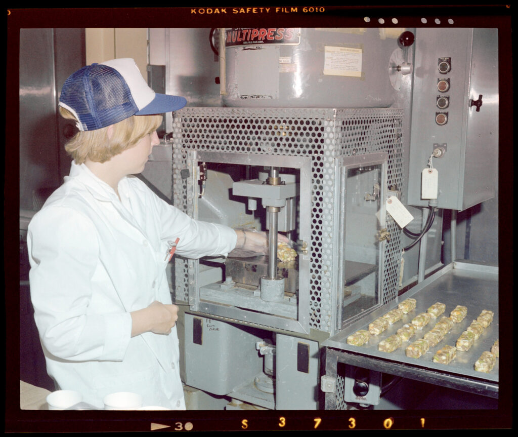 Woman wearing a lab coat and mesh cap loading a sample into a hydraulic press