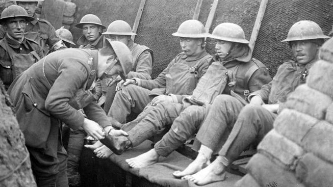 Old photo of soldiers in a World War I trench, one with his feet exposed.