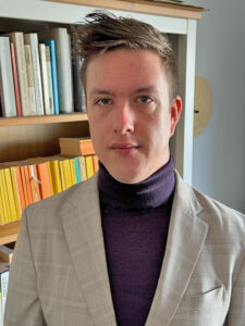 David Ragnar Nelson in a blazer and turtleneck in front of bookshelf